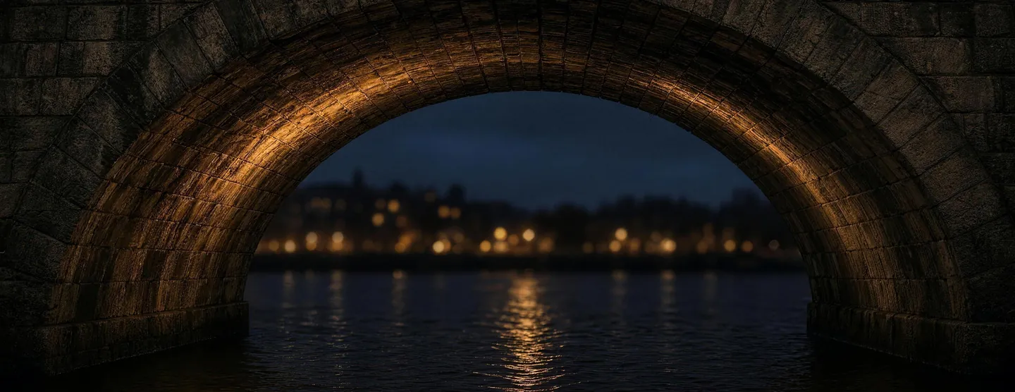 The underside of a stone bridge arch over a river at night, lit warm from below, with the lights of the far bank blurred beyond it.